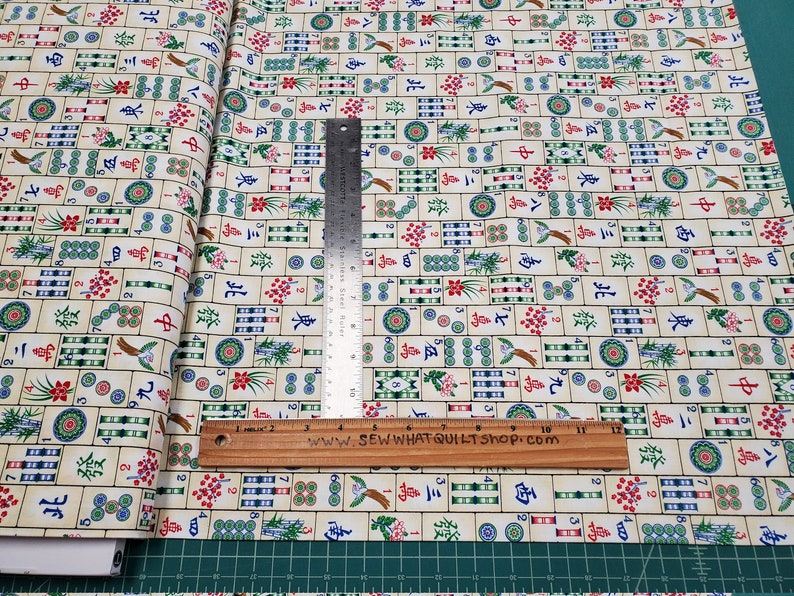 Puede incluir: Tela crema con un patr&oacute;n repetido de fichas de Mahjong coloridas. Las fichas presentan varios s&iacute;mbolos, n&uacute;meros e ilustraciones. Una regla met&aacute;lica y una regla de madera est&aacute;n colocadas sobre la tela. El texto "SEW WHAT QUILT SHOP.COM" es visible.