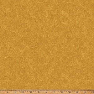 May include: A mustard yellow fabric featuring a repeating pattern of delicate, thin, light-colored swirls and small dots. A metal ruler is visible at the bottom edge, showing measurements in inches from 1 to 12 for scale and reference.