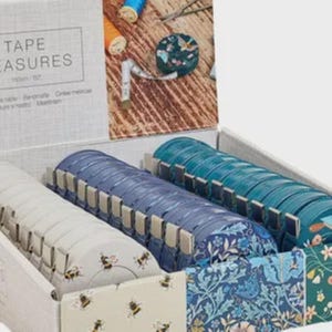 Puede incluir: Un juego de cintas métricas en una caja, con una variedad de colores y patrones. El juego incluye cintas métricas blancas, azules y turquesas, algunas con diseños florales y de abejas. La caja muestra el texto "TAPE MEASURES".