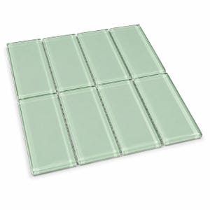 May include: A rectangular grid of eight light sage green glass tiles arranged in two rows of four. Each tile features a smooth, glossy surface with beveled edges and a translucent quality, creating a uniform and reflective appearance.