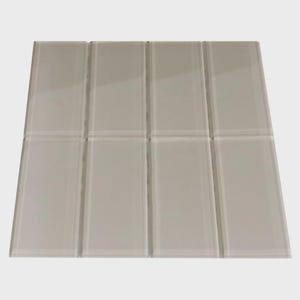 May include: A rectangular tile mosaic composed of eight rectangular tiles. The tiles are a light, neutral color, possibly off-white or a very light gray. The surface appears smooth and reflective, suggesting a glass or glazed finish. The tiles are arranged in a grid pattern.