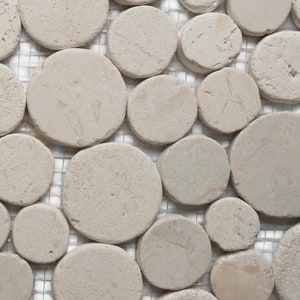 May include: Close-up of a mosaic tile pattern featuring irregularly shaped, light beige, circular stones. The stones are set against a white, grid-like background, creating a textured, natural stone appearance. Ideal for flooring or wall decor.