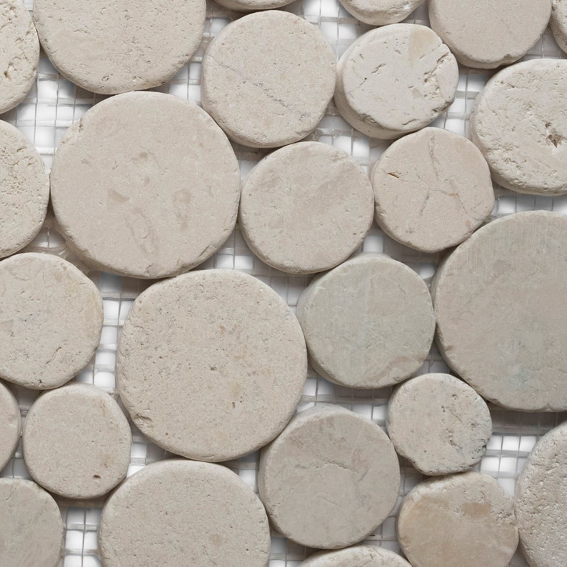 May include: Close-up of a mosaic tile pattern featuring irregularly shaped, light beige, circular stones. The stones are set against a white, grid-like background, creating a textured, natural stone appearance. Ideal for flooring or wall decor.