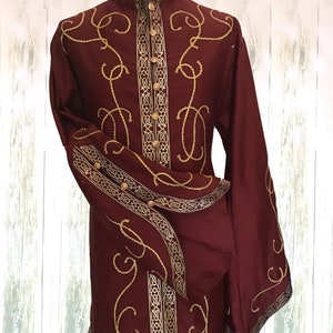 May include: A long-sleeved burgundy shirt with gold embroidery. The shirt has a high collar and a button-up front. The embroidery features a repeating pattern of swirls and lines.