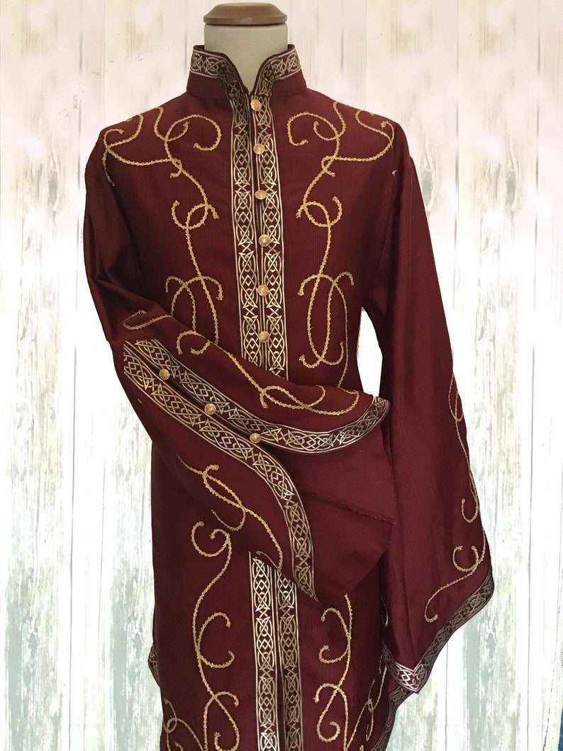 May include: A long-sleeved burgundy shirt with gold embroidery. The shirt has a high collar and a button-up front. The embroidery features a repeating pattern of swirls and lines.