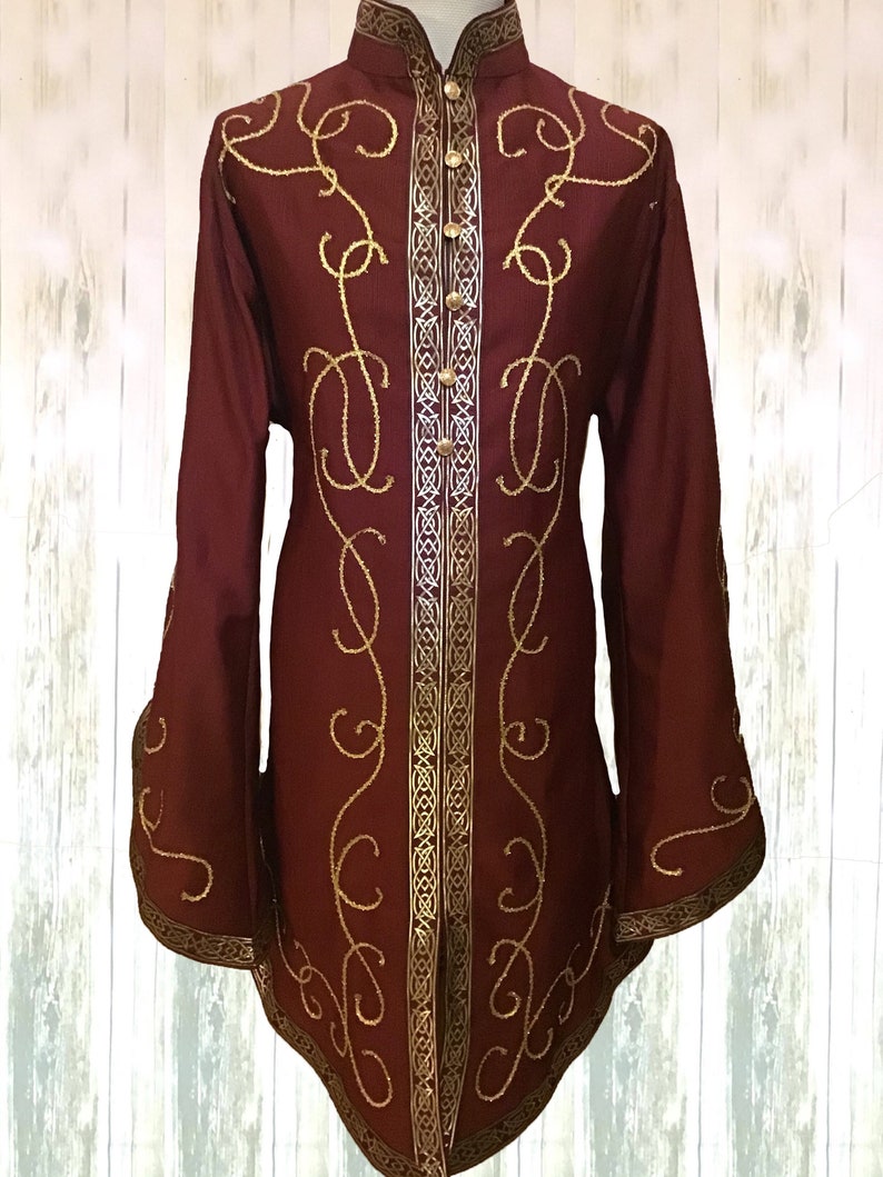 May include: A maroon long-sleeved shirt with gold embroidery and a high collar. The shirt has a button-up front and a decorative trim around the edges.