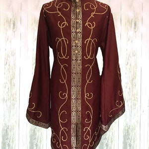 May include: A long-sleeved burgundy shirt with a high collar and gold embroidery. The embroidery features a repeating pattern of swirls and lines.