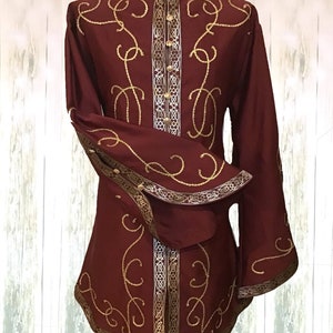 May include: A burgundy long-sleeved shirt with a high collar and gold embroidery. The shirt has a decorative trim around the collar, cuffs, and hem.