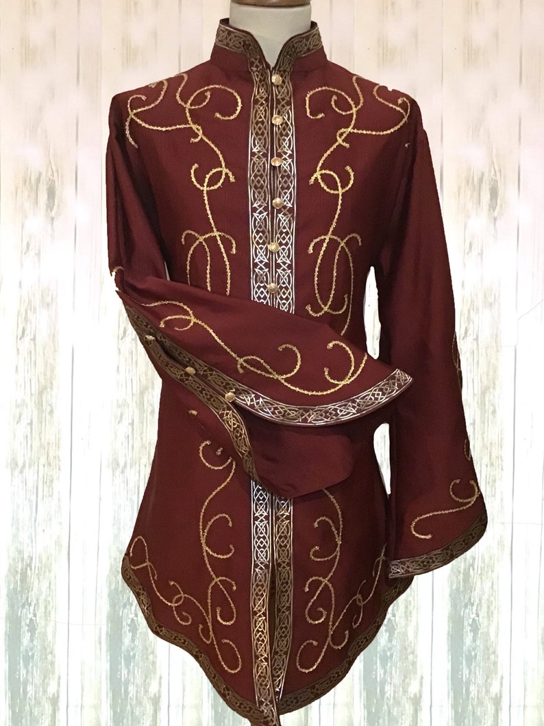 May include: A burgundy long-sleeved shirt with a high collar and gold embroidery. The shirt has a decorative trim around the collar, cuffs, and hem.
