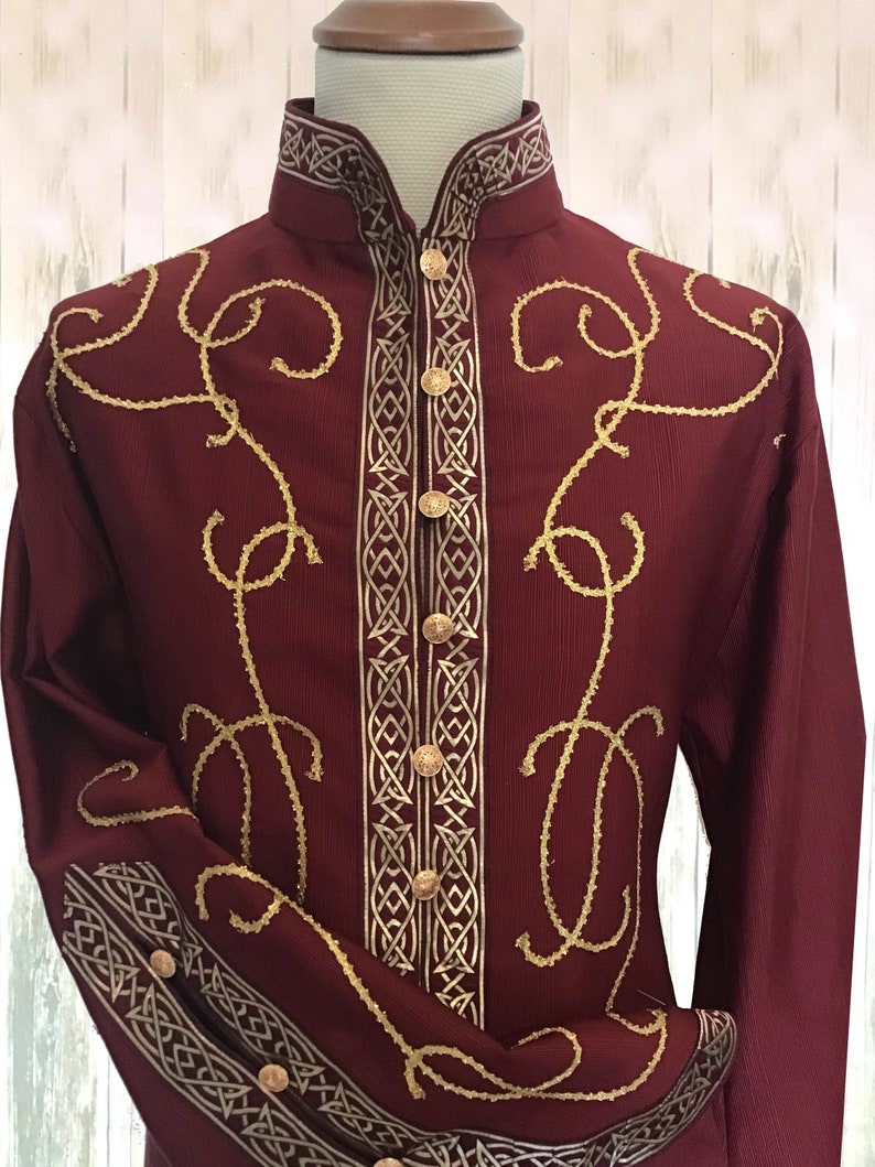 May include: A burgundy long-sleeve shirt with gold embroidery. The shirt has a mandarin collar and a button-up front. The embroidery features a Celtic knot design and intricate swirls.