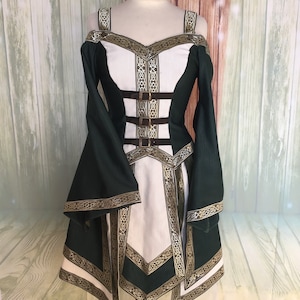 May include: A green and white medieval-style dress with gold trim and brown buckles. The dress has off-the-shoulder sleeves and a fitted bodice. The design includes intricate gold patterns along the edges and straps, creating a historical aesthetic.