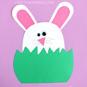 Peut inclure: Un lapin en papier blanc avec des oreilles roses et des yeux globuleux sort d'un nid de papier vert en forme d'herbe.