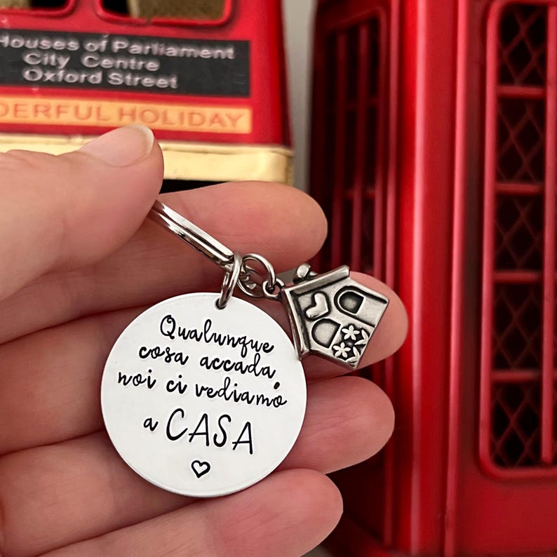 Puede incluir: Un llavero plateado con un dije redondo y un dije en forma de casa. El dije redondo tiene la frase italiana "Qualunque cosa accada noi ci vediamo a CASA" y un coraz&oacute;n. El dije de la casa tiene recortes decorativos.