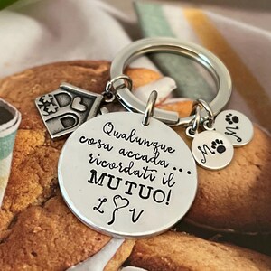 Puede incluir: Llavero plateado con m&uacute;ltiples colgantes. El colgante principal es un disco redondo con texto en italiano. Los colgantes adicionales incluyen una casa, huellas de patas e iniciales.