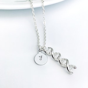 Puede incluir: Collar de plata con un dije de hélice de ADN y un dije redondo con la letra 'F' grabada.