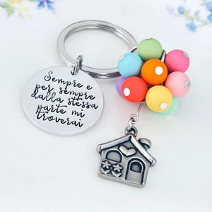 Peut inclure: Un porte-clés argenté avec un charm rond gravé de texte italien, un groupe de perles colorées et un petit charm en forme de maison. Les perles sont de différentes couleurs, dont le rose, le vert et l'orange. Le charm de la maison a des détails de cœur et de fleurs.