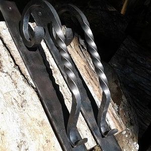 May include: Two hand-forged metal door pulls. Each pull features a flat, rectangular base with mounting holes and a decorative, twisted handle. The handles have a scroll design at the top. The metal has a dark, matte finish.