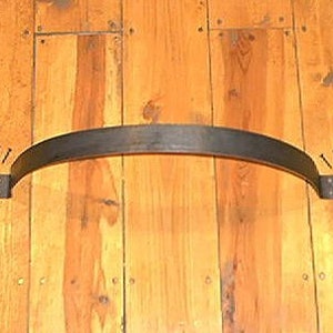 May include: A black, curved metal door pull with decorative fleur-de-lis ends. The pull is mounted on a wooden door with visible wood grain and is secured with screws. This rustic hardware adds a touch of vintage charm.