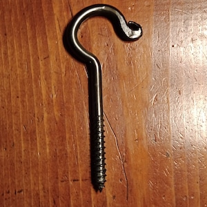 May include: A black metal screw-in ceiling hook. The hook has a curved design with a pointed screw end for easy installation. The hook is designed to hold items from the ceiling.