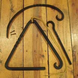 May include: Black metal triangle musical instrument with a curved hanger, a striker, and a curved hook. The triangle is suspended by a yellow cord. Two small screws are also present. The items are on a wooden surface.