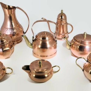 May include: A set of eight copper kitchenware items, including a pitcher, a teapot, a kettle, and four sugar bowls. The items are all made of hammered copper and have brass accents.