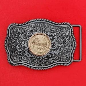 Puede incluir: Una hebilla de cinturón de plata con un diseño ornamentado que presenta una moneda de oro con el retrato de un hombre y las palabras "United States of America" y "Sequoyah".