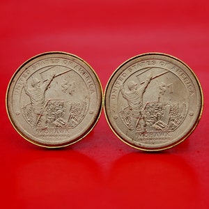 May include: Two gold-colored US dollar coins with the inscription "United States of America" and "Mohawk Iron Workers" on the back. The front of the coins depict a worker holding a beam.
