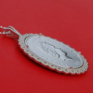 May include: A silver pendant necklace featuring a silver coin with a profile of Queen Elizabeth II. The coin is dated 2005 and has a decorative border.