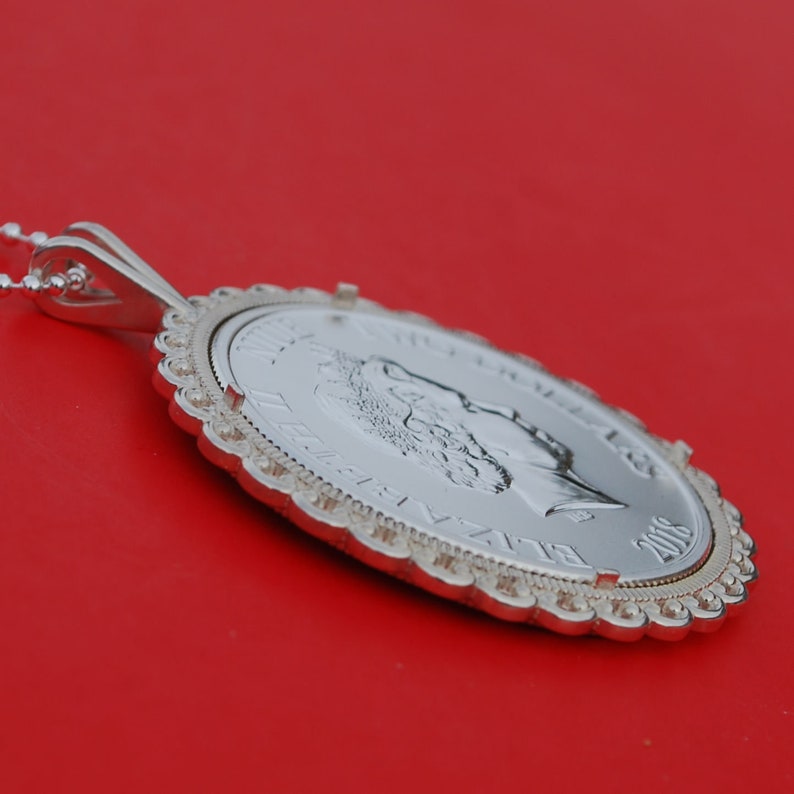 May include: A silver pendant necklace featuring a silver coin with a profile of Queen Elizabeth II. The coin is dated 2005 and has a decorative border.