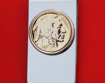 May include: A silver money clip with a gold-toned 1957 Buffalo nickel coin design. The coin features a profile of an American Indian with the word "LIBERTY" inscribed on the coin.