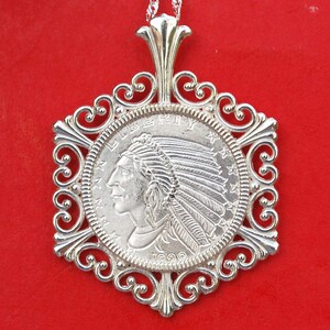 May include: Silver pendant necklace featuring a 1920 Indian Head coin with a decorative filigree frame. The coin depicts a profile of an indigenous person wearing a headdress.