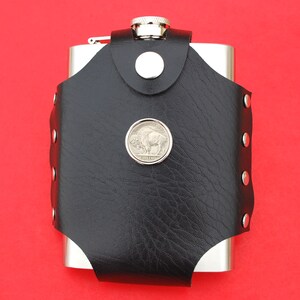 May include: A silver flask with a black leather cover and a silver buffalo nickel design. The flask has a snap closure and is decorated with silver studs.