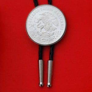 May include: A silver bolo tie featuring a Mexican 25 Peso coin with an eagle design and the text "ESTADOS UNIDOS MEXICANOS" and "LEY .720" around the edge.
