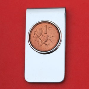 May include: A silver money clip with a 1 cent coin from New Zealand featuring two birds on a branch. The coin is copper colored.