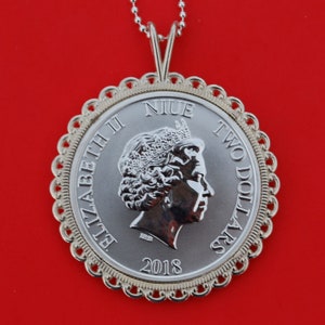 May include: Silver coin pendant with a portrait of Queen Elizabeth II and the text "NIUE TWO DOLLARS 2018". The coin is surrounded by a decorative gold-colored border.