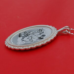 May include: Silver pendant featuring a Mickey Mouse and Minnie Mouse design with Chinese characters. The pendant has a scalloped edge and is on a red background.