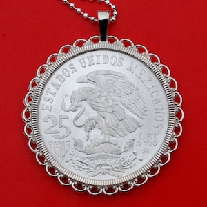Op de afbeelding: Een zilveren ketting met een hanger met een Mexicaanse 25 Peso-munt met een adelaar en slang ontwerp. De munt is omgeven door een decoratieve rand en hangt aan een zilveren ketting.