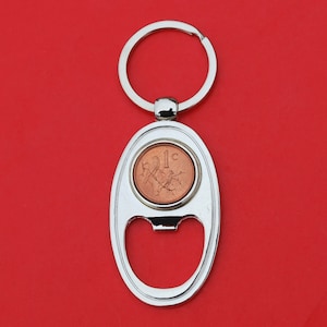 May include: Silver key chain with a bottle opener and a 1c coin from Ireland. The coin is in the center of the key chain and is surrounded by a silver ring.