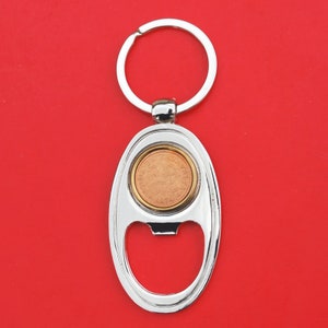 May include: Silver bottle opener keychain with a round coin-shaped insert featuring a copper-colored design. The keychain has a silver ring.