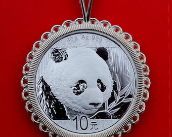 May include: A silver pendant featuring a Chinese panda coin with the inscription "30g Ag 999 10元". The coin is surrounded by a decorative silver frame and hangs from a silver chain.