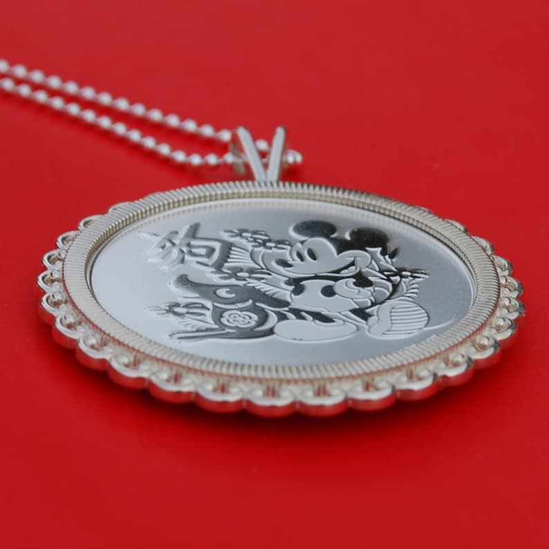 May include: Silver pendant necklace featuring a Mickey Mouse design with Chinese characters. The pendant is round and has a scalloped edge.