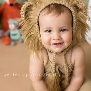 May include: A smiling baby wearing a tan lion costume, including a furry hood with braided trim and a matching jumpsuit. The background includes stuffed animals and the text "picture perfect photography".