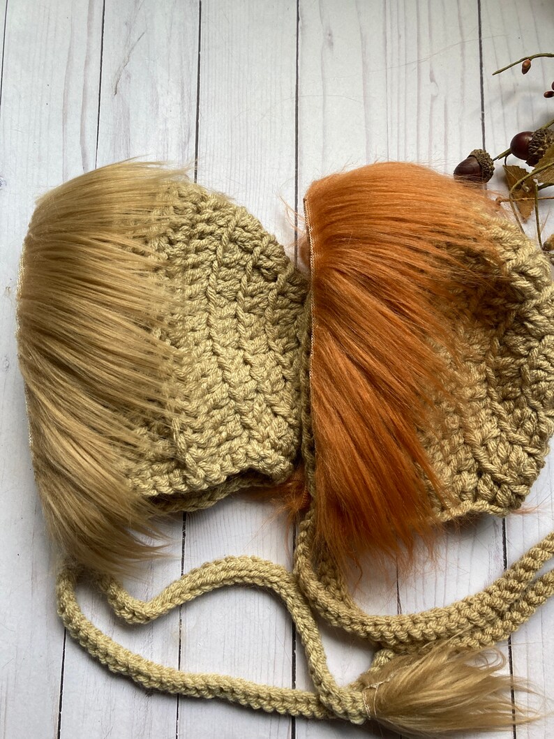 May include: Two handmade crochet baby hats, one with light brown faux fur and the other with orange faux fur. The hats are a light tan color and have long ties. The hats are designed to look like a lion's mane.