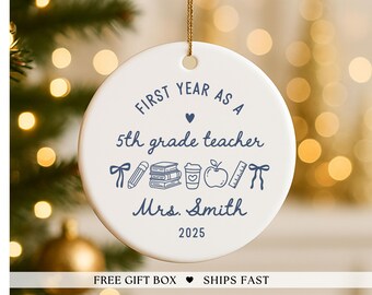 May include: White ceramic ornament with a gold string, featuring blue text and illustrations. The text reads "FIRST YEAR AS A 5th grade teacher Mrs. Smith 2025." Includes a pencil, books, coffee cup, apple, and ruler.