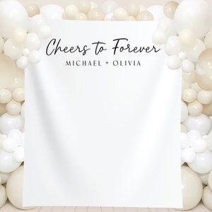 K&ouml;nnte beinhalten: Wei&szlig;er Hintergrund mit dem Text "Cheers to Forever" und den Namen "Michael + Olivia" in schwarzer Schrift. Der Hintergrund ist mit einer Girlande aus wei&szlig;en und cremefarbenen Ballons verziert.