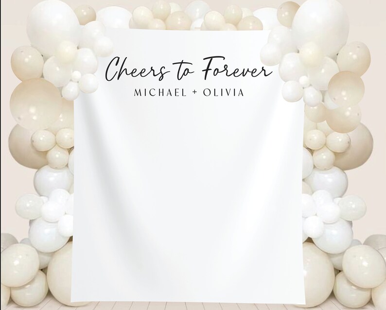 K&ouml;nnte beinhalten: Wei&szlig;er Hintergrund mit dem Text "Cheers to Forever" und den Namen "Michael + Olivia" in schwarzer Schrift. Der Hintergrund ist mit einer Girlande aus wei&szlig;en und cremefarbenen Ballons verziert.