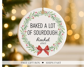 May include: A white ceramic Christmas ornament with the text "BAKED A LOT OF SOURDOUGH" in black, surrounded by a green and red wreath. The name "Rachel" and the year "2025" are below the text, with a red bow at the bottom.
