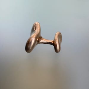 May include: A pair of silver cufflinks with an abstract, organic design. The cufflinks are made of smooth, polished metal and have a modern, minimalist aesthetic.