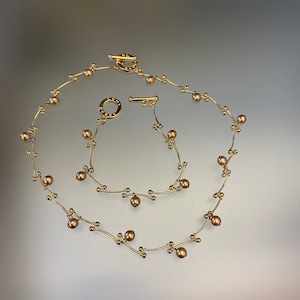 May include: A gold necklace featuring small, round, brown beads. The necklace is crafted from delicate, twisted wire and has a clasp fastening.
