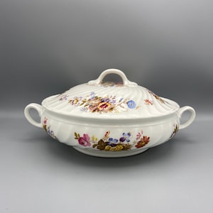 May include: White ceramic serving dish with a lid. The dish features a floral pattern in shades of pink, blue, yellow, and brown. The lid has a fluted design.